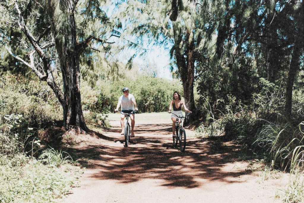 A couple biking on a shaded resort trail in Oahu, surrounded by lush greenery—perfect for a relaxing Oahu itinerary for Introverts and HSPs.