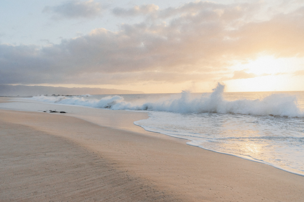 An empty beach in Oahu at sunrise, with soft pastel skies and calm ocean waves—perfect for a relaxing Oahu itinerary.