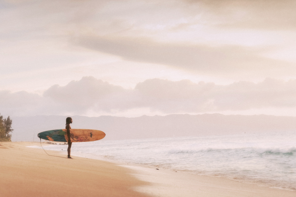 A quiet sunset walk on the beach in Oahu, with one surfer about to enter the water—perfect for a relaxing Oahu itinerary