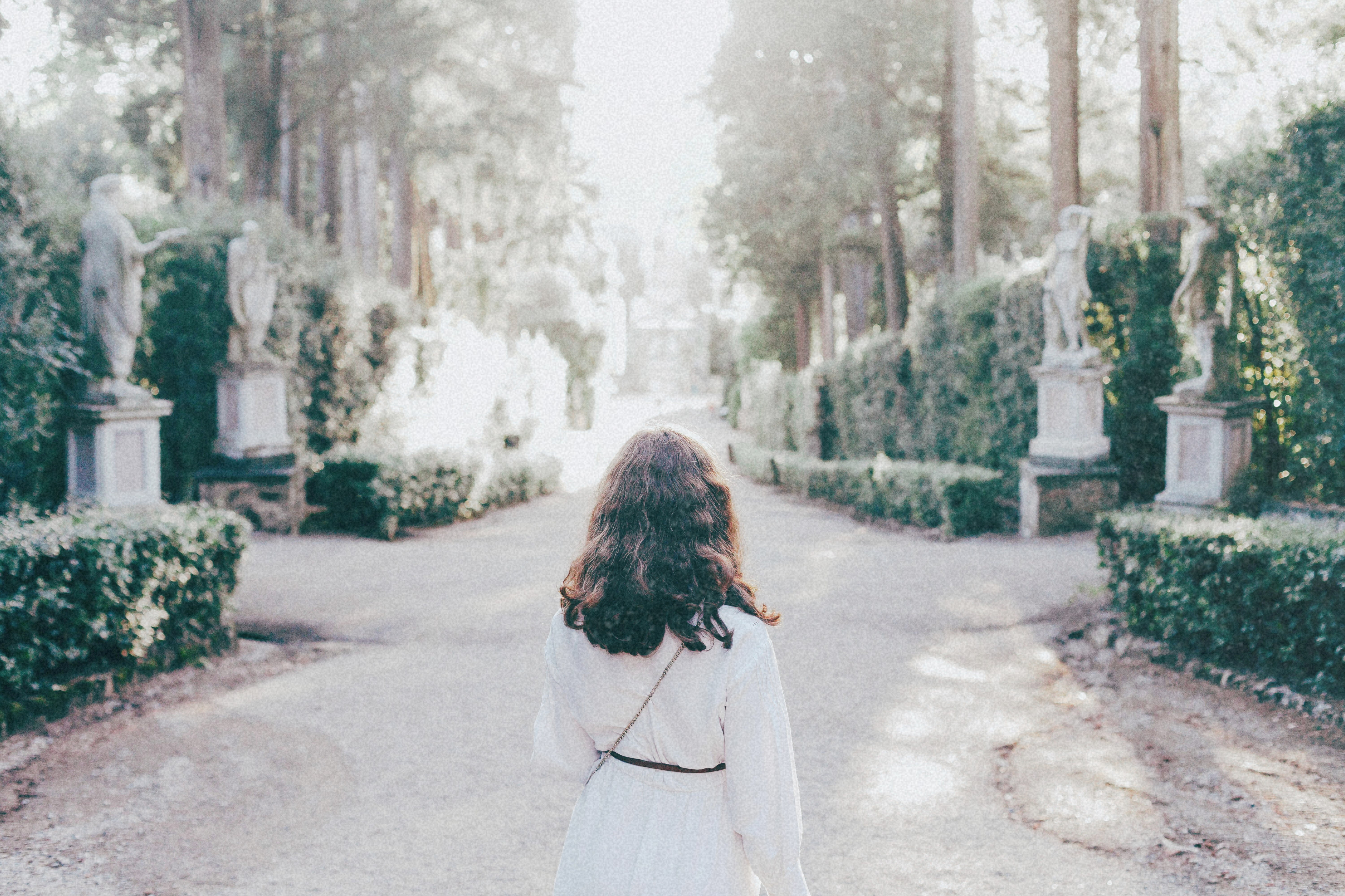 A woman peacefully wandering through a lush garden, looking refreshed and well-rested after a long journey.